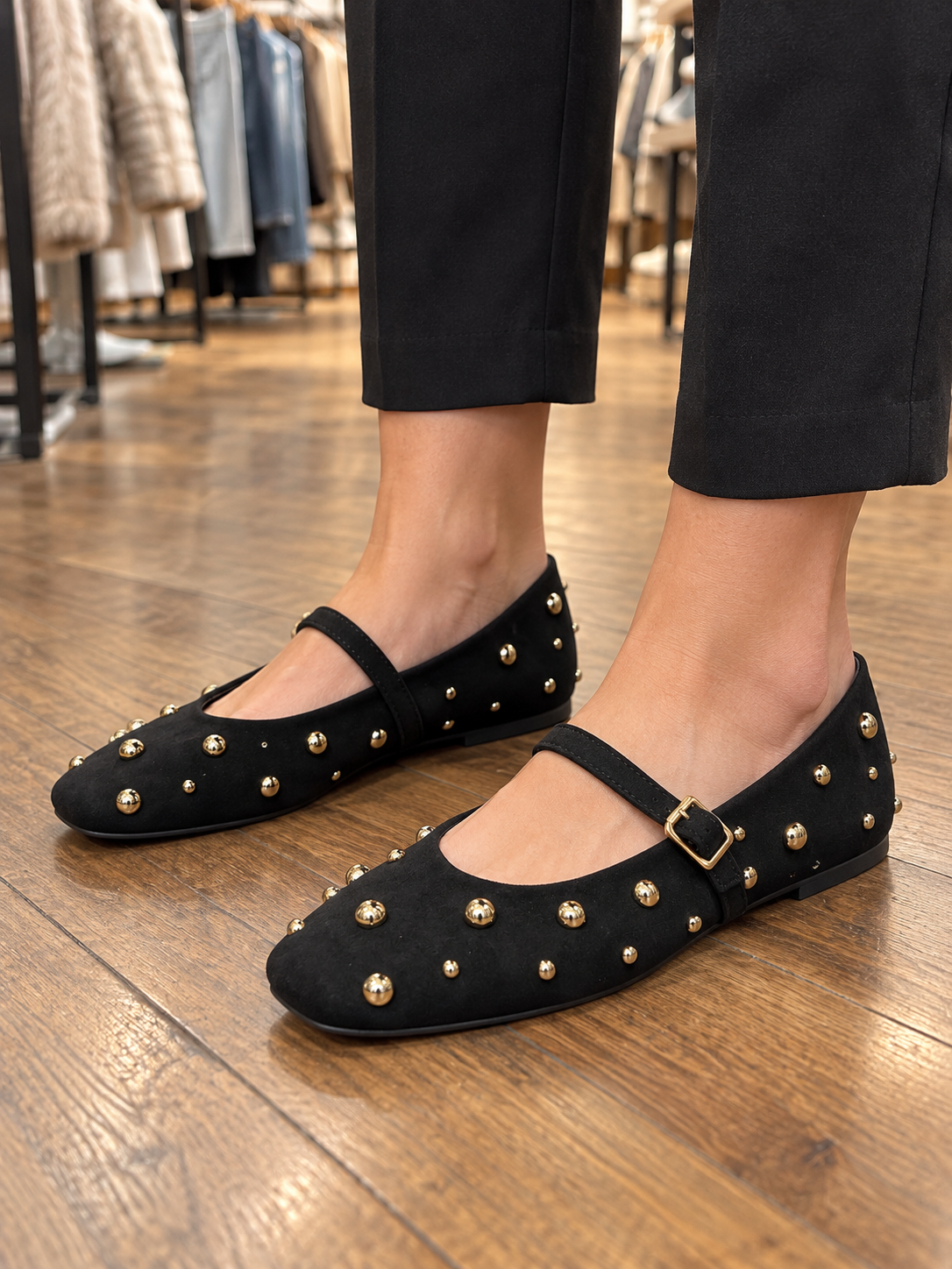 Ballerines noires d’aspect suédé à bride et clous dorés, portées en boutique KIFFEUR